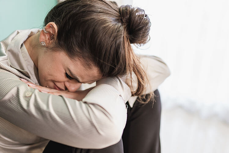 Eine Frau mit gesenktem Kopf und stützt sich auf die Arme – Ausdruck von Überforderung und Kummer